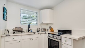 Una cocina compacta con armarios blancos, un horno negro, un tostador y una ventana con persianas.