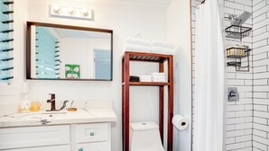 Un baño con inodoro blanco, estante de madera con toallas, espejo con luces y pared de azulejos.