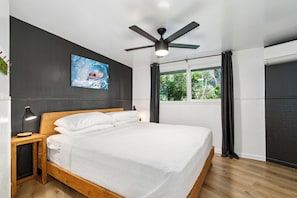 Ein modernes Schlafzimmer mit einem Holzbett, einem Deckenventilator, einem großen Fenster mit Vorhängen und einem Wandbild.