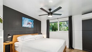 Ein modernes Schlafzimmer mit einem Holzbett, einem Deckenventilator, einem großen Fenster mit Vorhängen und einem Wandbild.