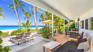 Ein überdachter Außenbereich mit Blick auf den Strand, Liegestühle, ein Tisch und eine Couch.