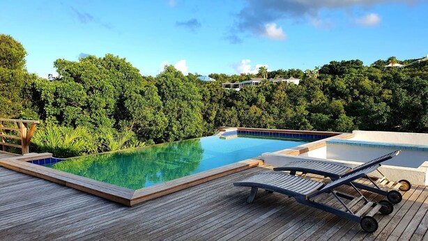 Eine Holzterrasse mit Pool, Liegestühlen und Blick auf eine üppige grüne Landschaft.