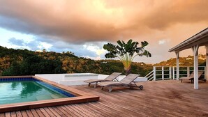 Eine Holzterrasse mit Pool, Liegestühlen und Blick auf einen Hügel mit Bäumen.