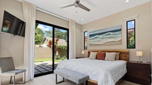 Un dormitorio con una cama grande, un banco, un televisor y vistas al exterior.