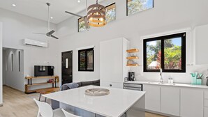 Una cocina moderna con una isla central, muebles blancos y un amplio ventanal con vistas a la vegetación.