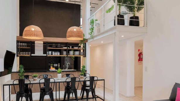 A modern kitchen with a dining area, featuring a high ceiling, pendant lights, and a view of the upper floor. - MOT Rentals + Villa Embajada - 6 Bd pax Deluxe House Belgrano (Buenos Aires)