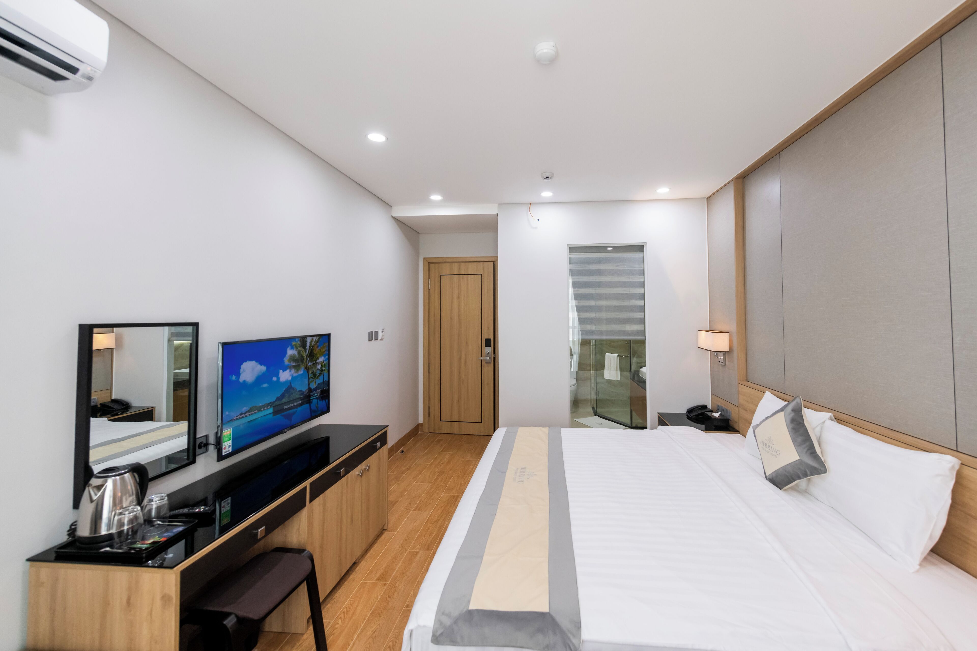 A modern hotel room with a bed, a desk with a computer, a television, and a mirror.