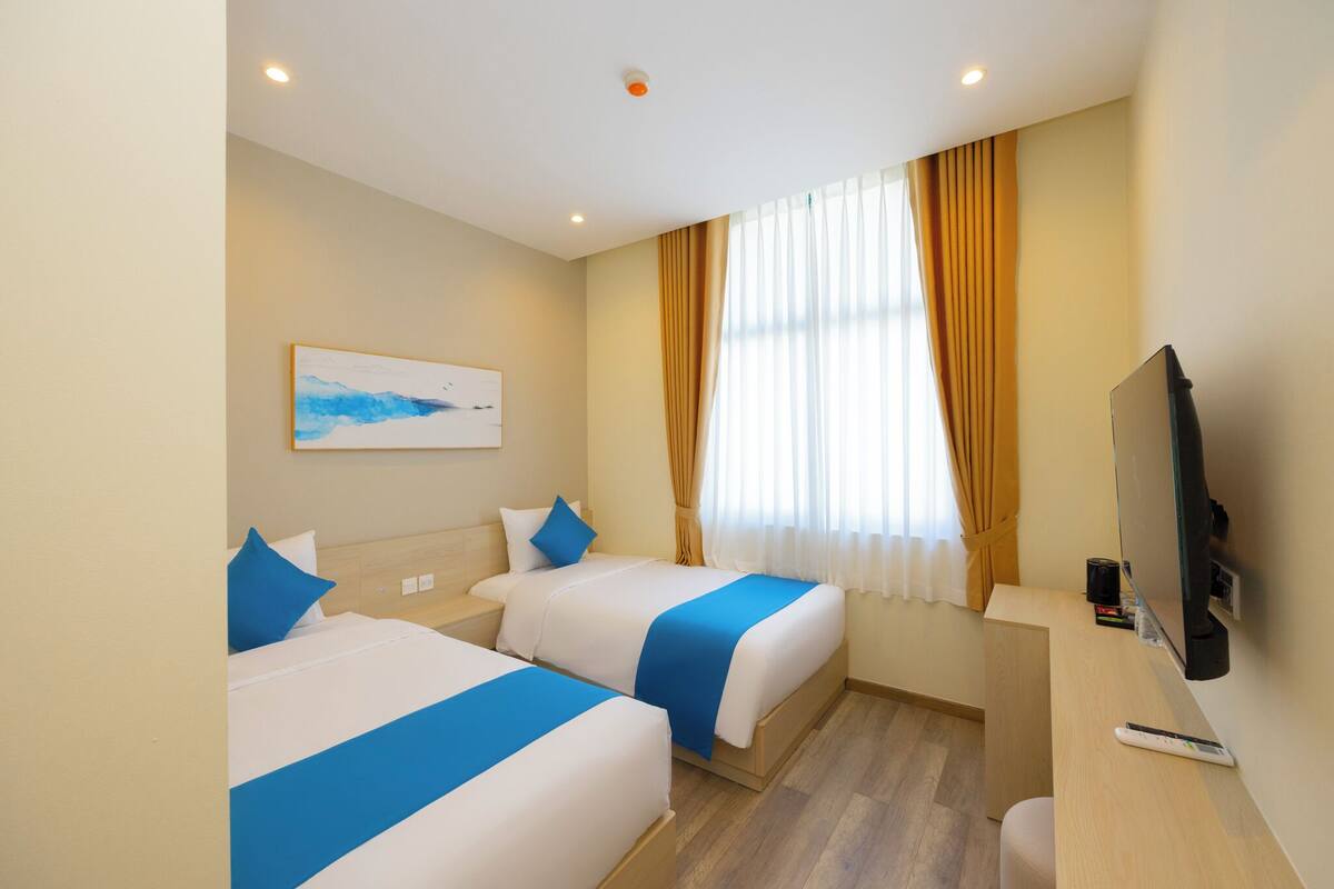 Une chambre d’hôtel avec deux lits, un bureau, une télévision et une fenêtre avec des rideaux.