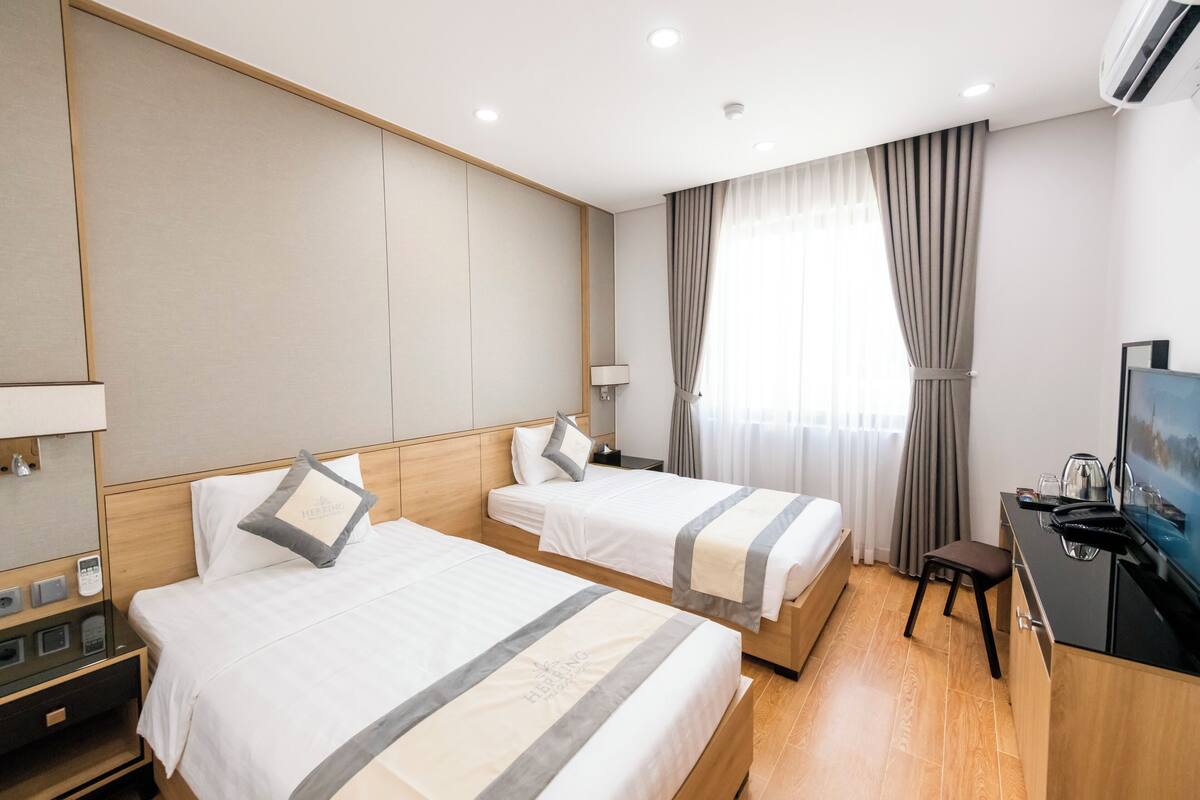 Une chambre d’hôtel avec deux lits, un bureau, une télévision et une fenêtre avec des rideaux.