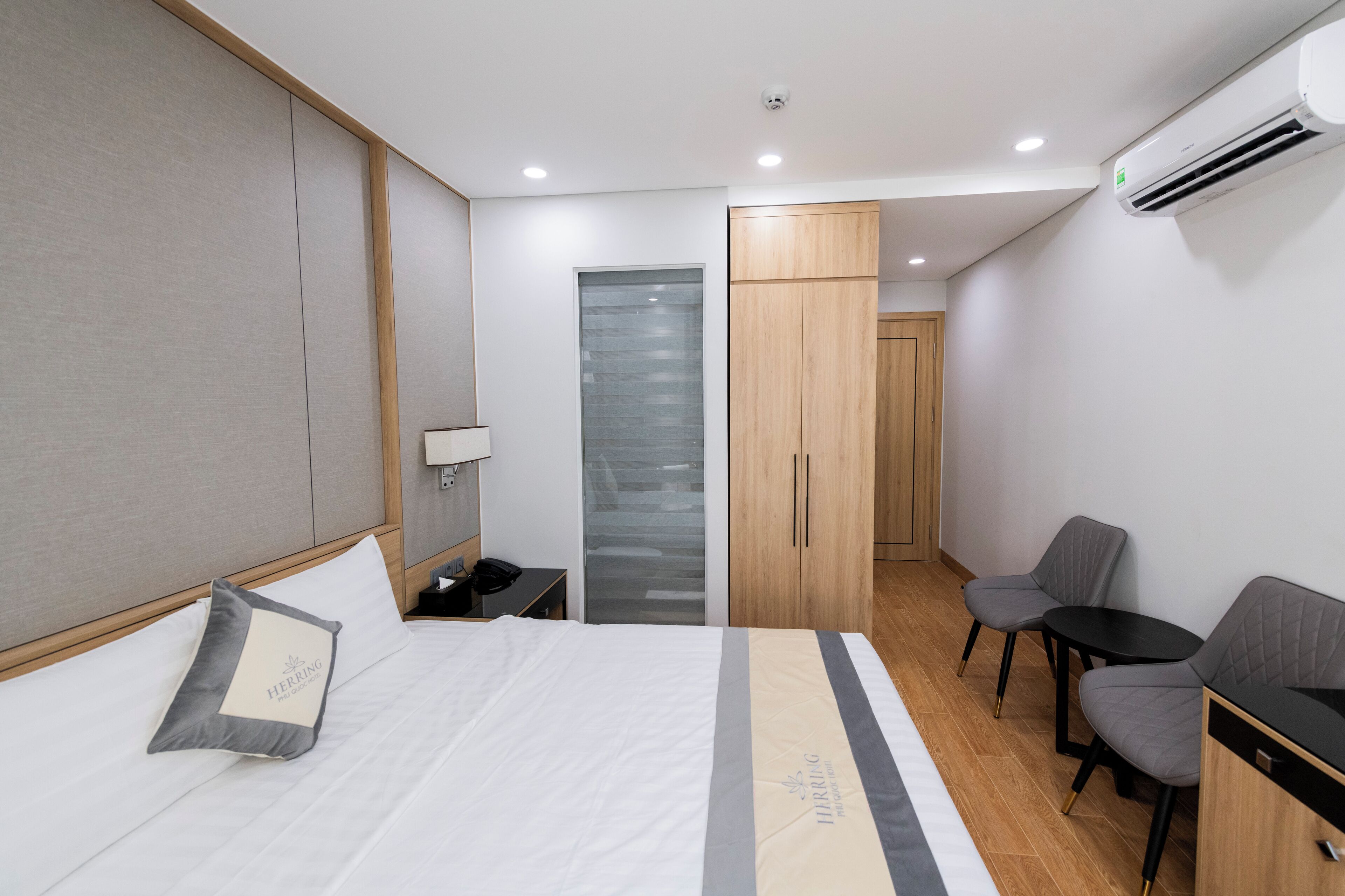Una camera d'albergo con un letto, una scrivania, due sedie, un armadio e un condizionatore d'aria.