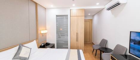 A hotel room with a bed, a desk, a chair, a TV, and a wardrobe.