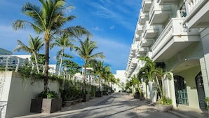 Een hotelgang met palmbomen, een witte gevel en een helderblauwe lucht.