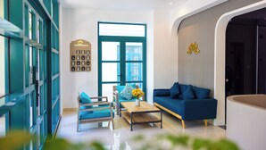 Een moderne woonkamer met een blauwe bank, een houten salontafel en een blauwe fauteuil. Er is een groot raam met uitzicht op de stad.