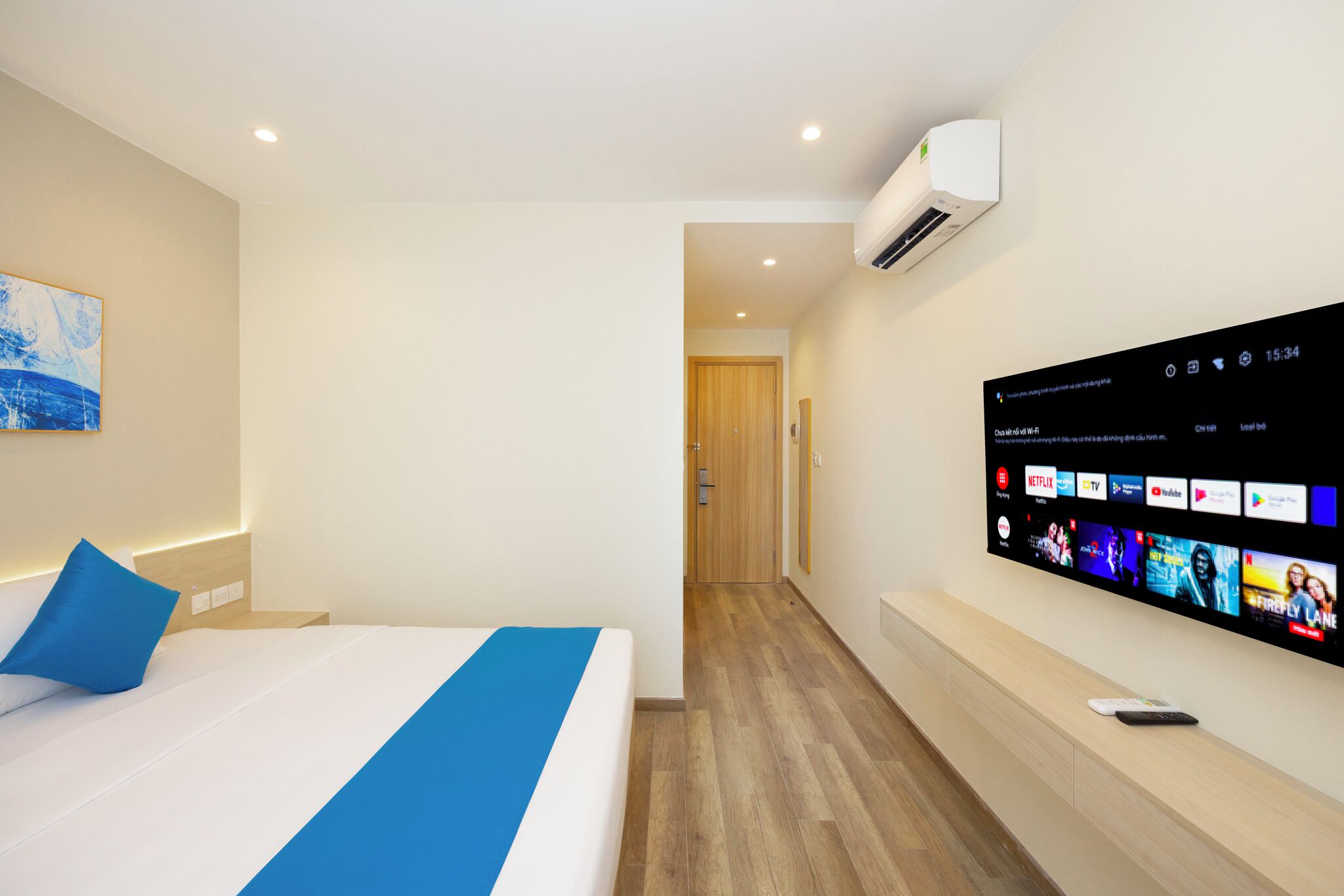 A hotel room with a bed, a TV mounted on the wall displaying various channels, and a hallway leading to another room.