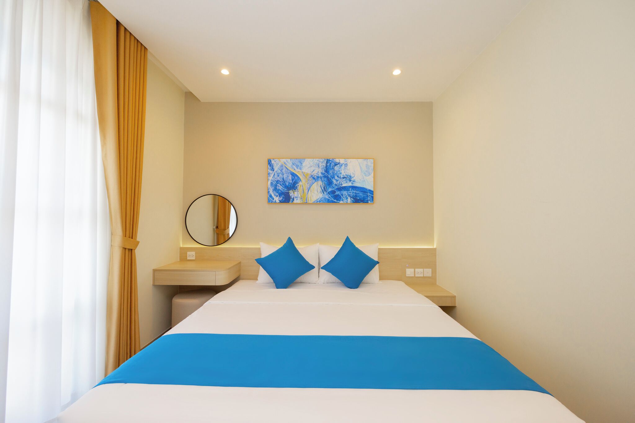 Una habitación de hotel con cama, mesita de noche, espejo y un cuadro en la pared.