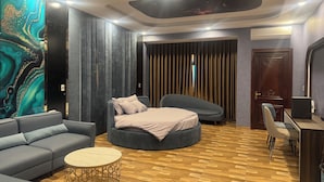 A modern bedroom with a grey sofa, a round bed, a small table, and a wall with a decorative painting. - Heaven Hotel (Vu Ninh)