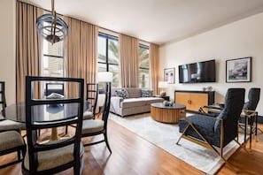 A modern living room with a glass dining table, a sofa, a coffee table, and a TV mounted on the wall. - 4BR Group Getaway Walk to French Quarter The Mayfair (New Orleans)
