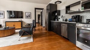 A modern kitchen with dark cabinetry, stainless steel appliances, and a wooden dining area. - 4BR Group Getaway Walk to French Quarter The Mayfair (New Orleans)