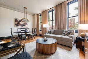 A modern living room with a sofa, coffee table, and dining area. - 4BR Group Getaway Walk to French Quarter The Mayfair (New Orleans)