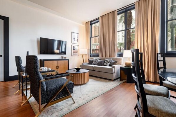 A modern living room with a sofa, armchairs, a TV, and a large window with curtains. - 4BR Group Getaway Walk to French Quarter The Mayfair (New Orleans)
