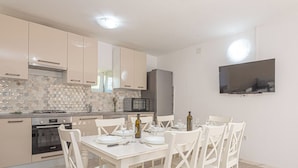 Une cuisine moderne avec des meubles blancs, une cuisinière à gaz, un four à micro-ondes et une table à manger pour quatre personnes.