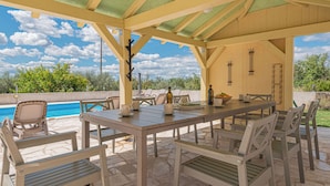 Une terrasse extérieure avec une piscine, une table à manger, des chaises et une pergola.