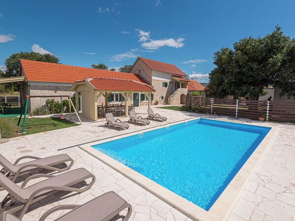 A swimming pool with lounge chairs, a covered seating area, and a stone building with a red-tiled roof. - Rural Villa Olive Krka by Interhome (Oklaj)