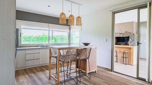 Una cocina moderna con un amplio ventanal, una chimenea de piedra y un comedor con sillas de mimbre.