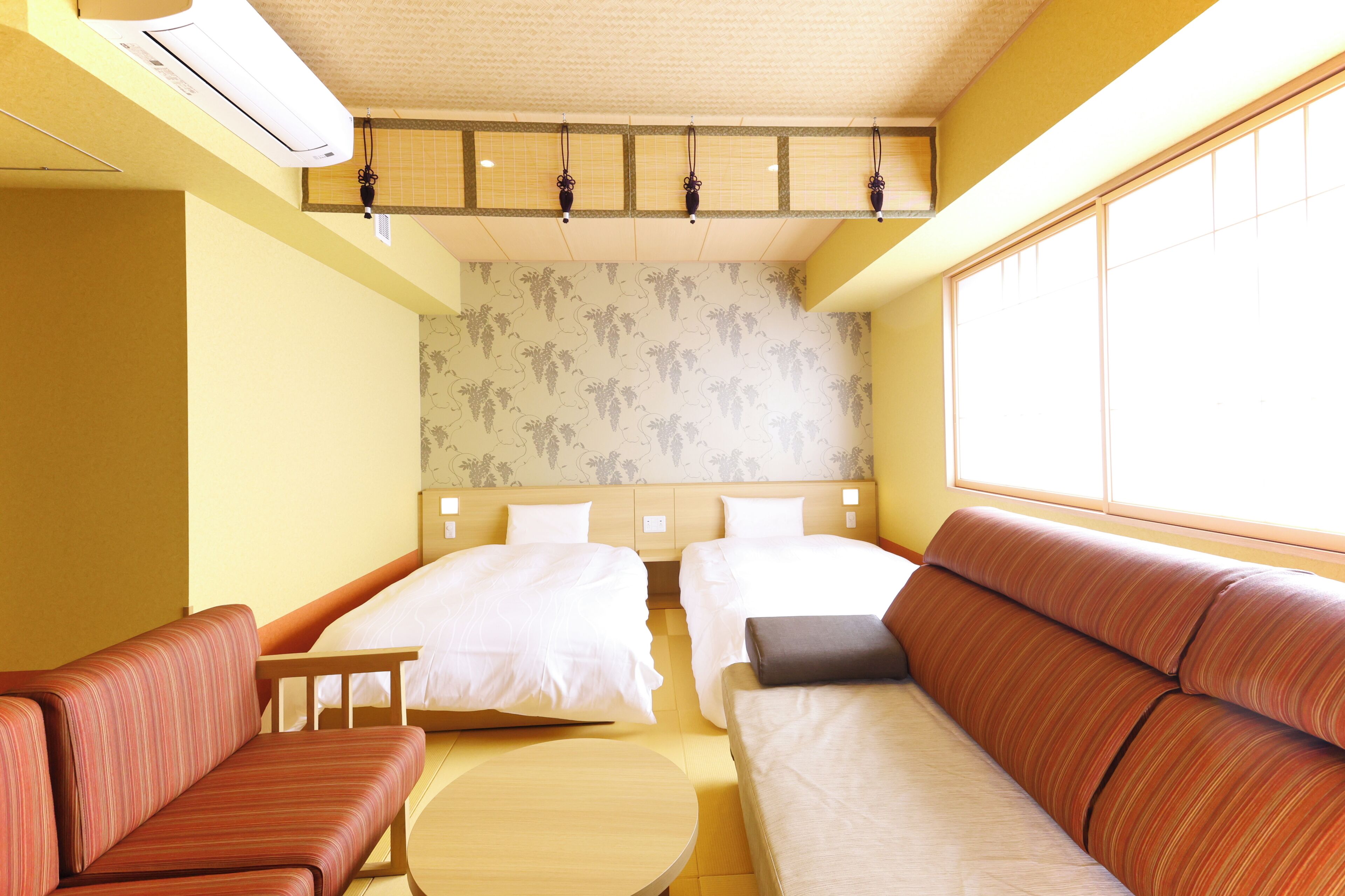 A hotel room with two beds, a sofa, a small table, and a large window.