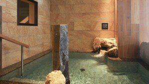 Zona de spa con pared de piedra, banca de madera y señal que indica aguas termales.