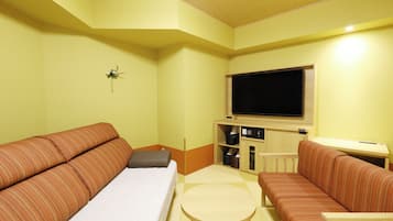 A hotel room with a large bed, two sofas, a small table, and a TV.