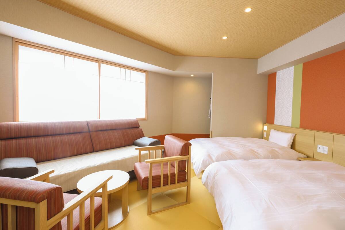 Ein Hotelzimmer mit einer Couch, zwei Einzelbetten, einem Holzstuhl und einem kleinen Tisch.