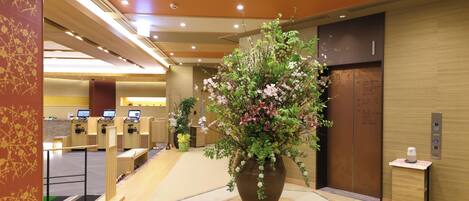 A reception area with a large floral arrangement, a reception desk, and an elevator.