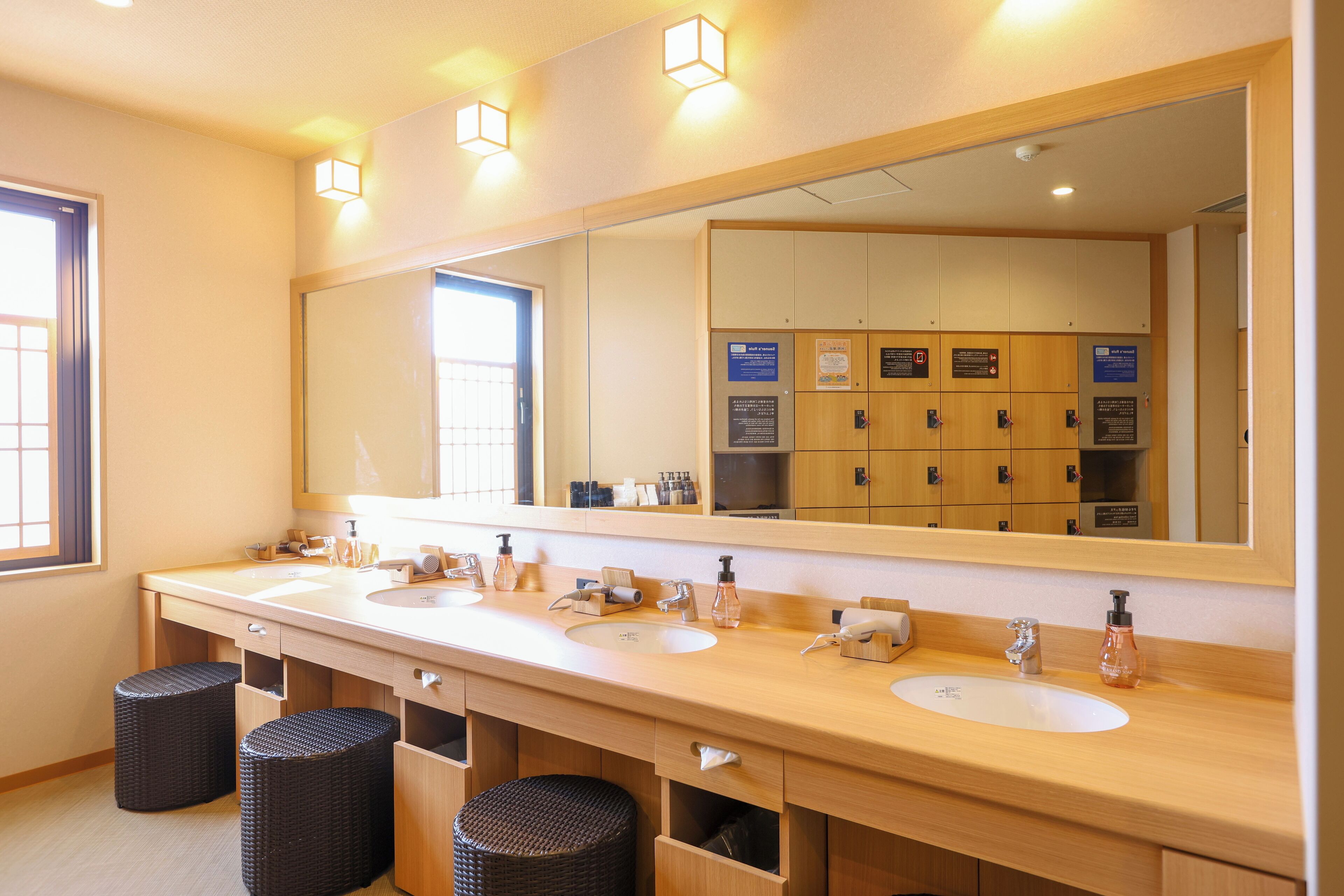 A hotel bathroom with two sinks, a large mirror, and a row of lockers.