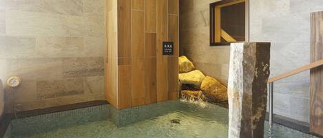A stone-walled bathroom with a wooden panel and a sign indicating a hot spring.