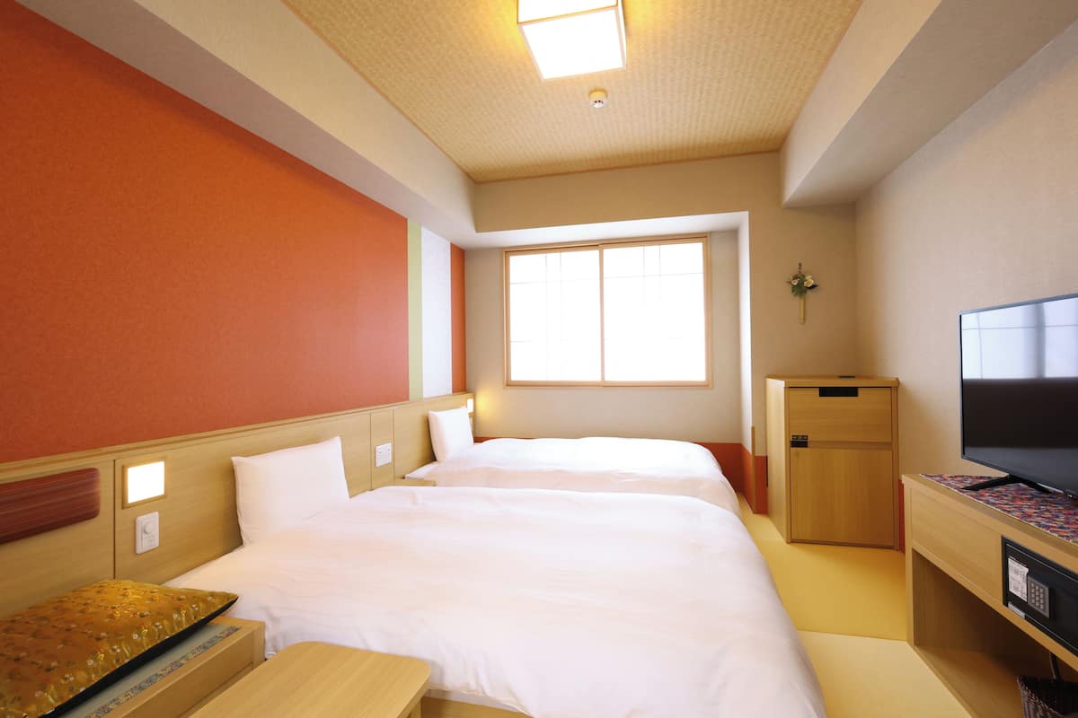 Ein Hotelzimmer mit zwei Betten, einem Fernseher, einem Schreibtisch und einem Fenster.