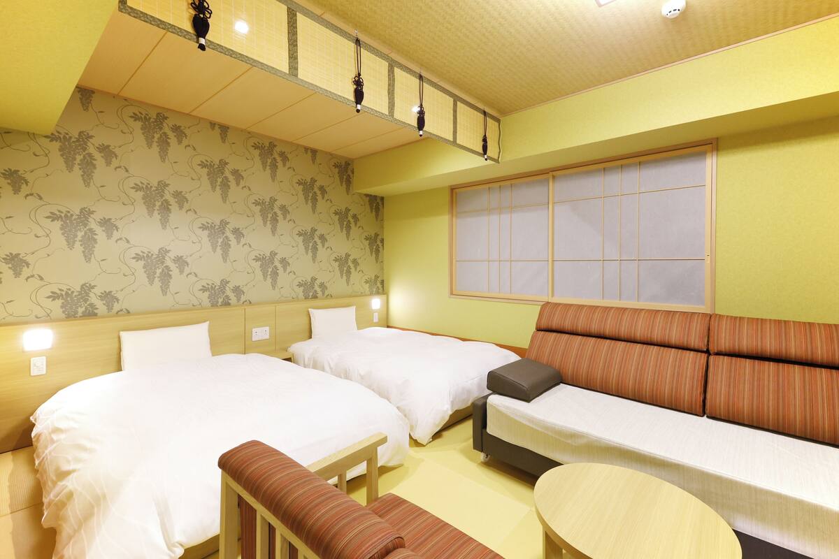 Ein Hotelzimmer mit zwei Betten, einem Schlafsofa, einem kleinen Tisch und einem Fenster mit Blick.