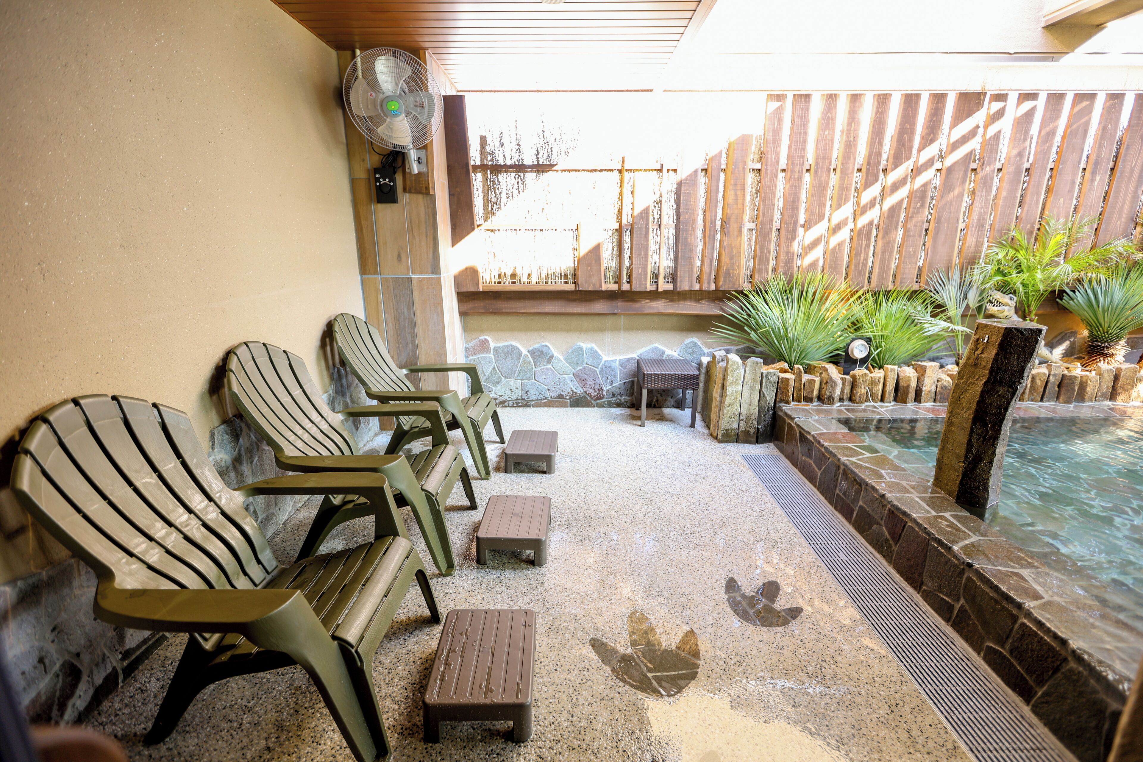 Un espace aménagé au bord de la piscine, avec des chaises longues, une petite table et un ventilateur.