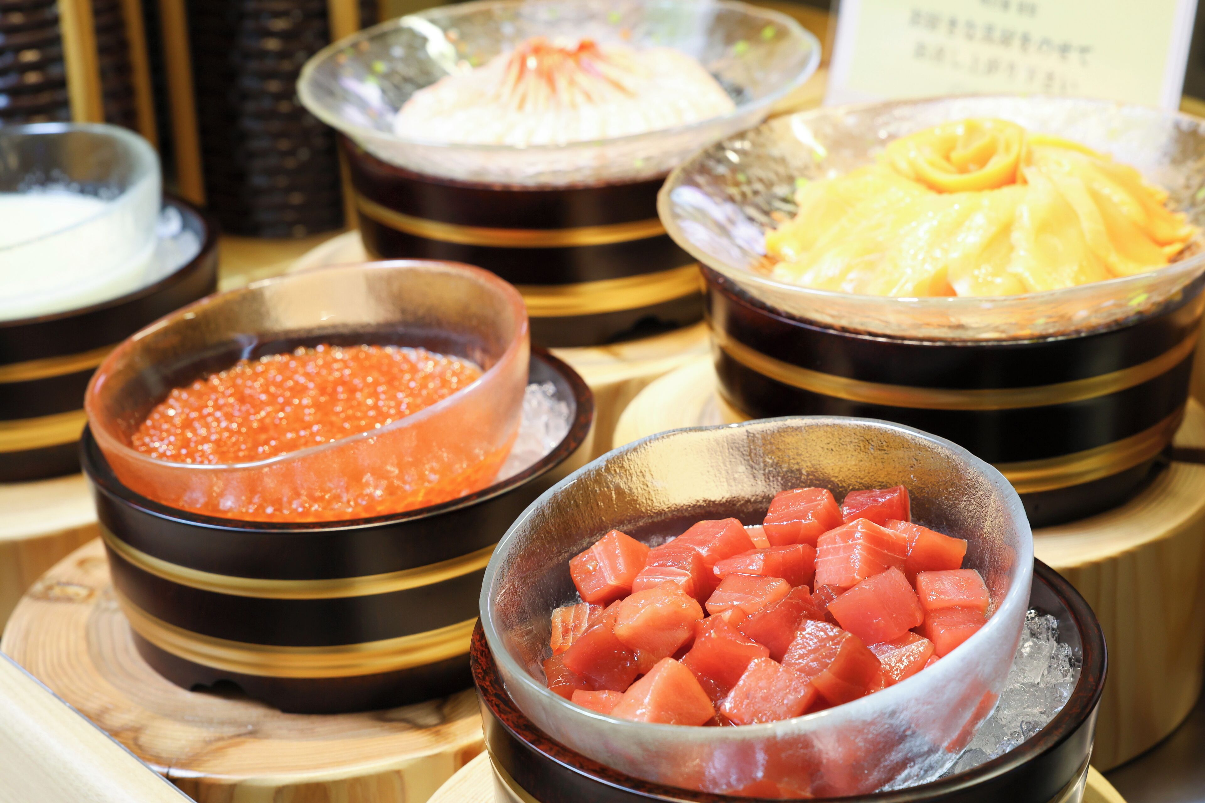A selection of food items in bowls, including what appears to be caviar, diced tomatoes, and a yellow fruit compote, served on a wooden table.