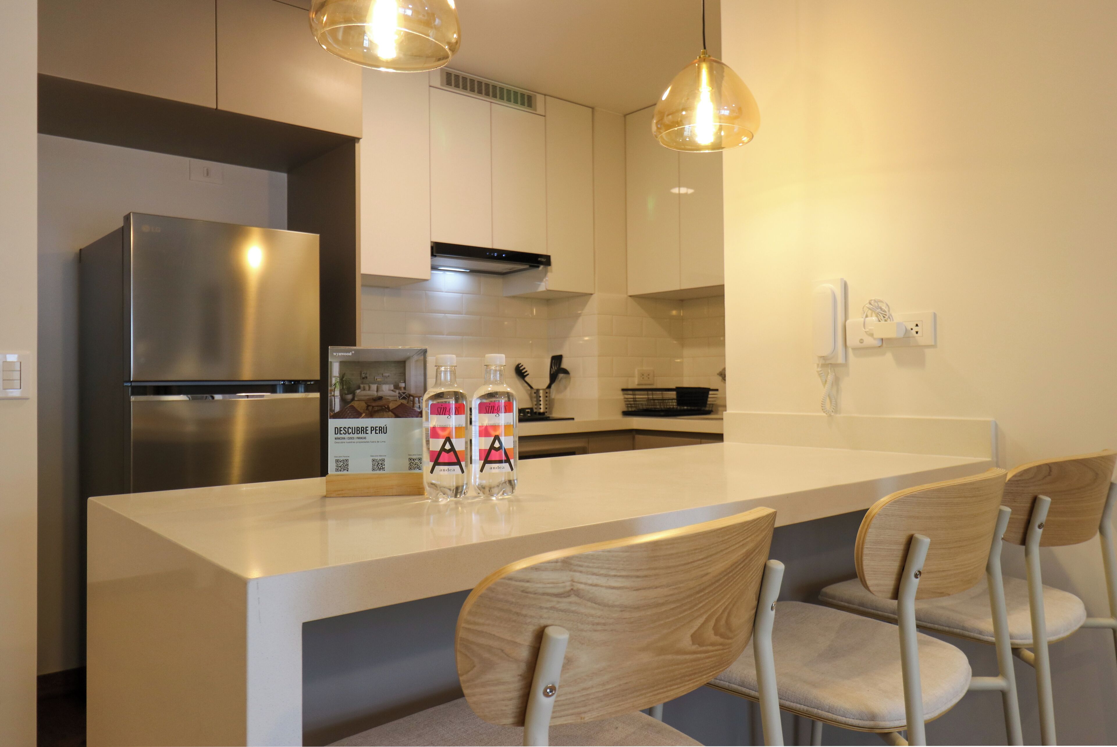 Eine moderne Küche mit einem Edelstahl-Kühlschrank, einer weißen Arbeitsplatte und Holzstühlen.