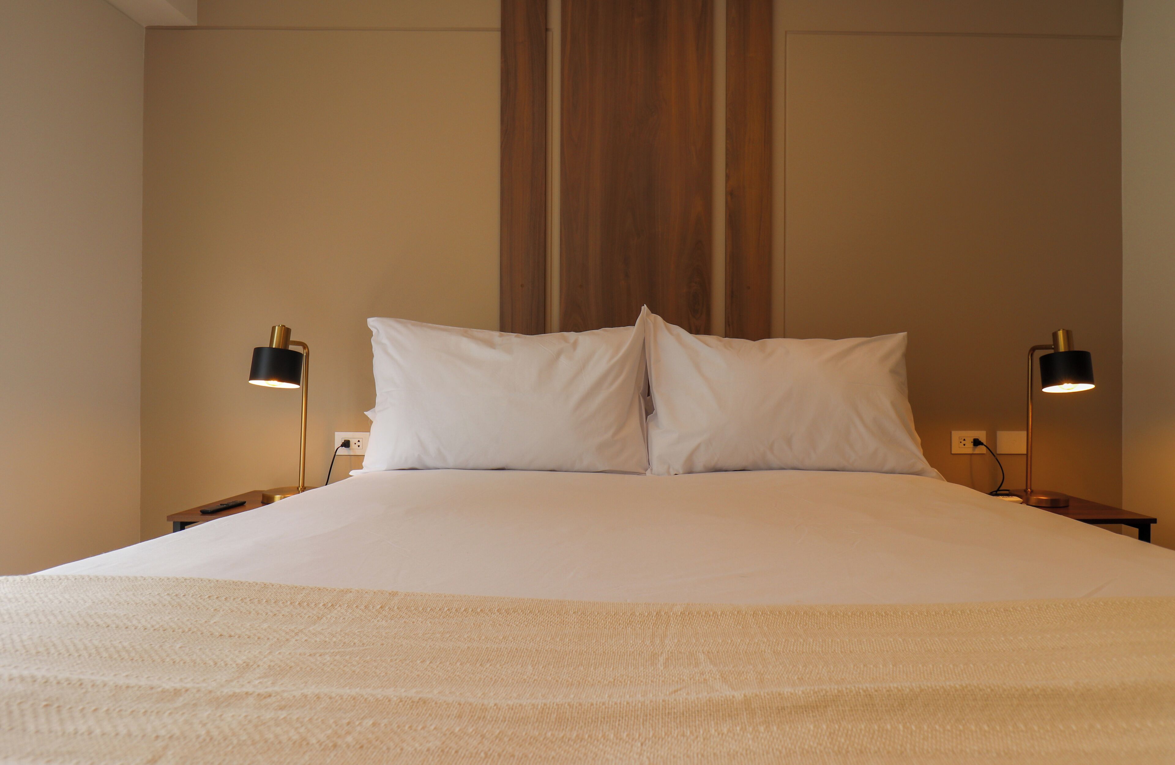 Una cama bien tendida con sábanas blancas y dos lámparas de noche.