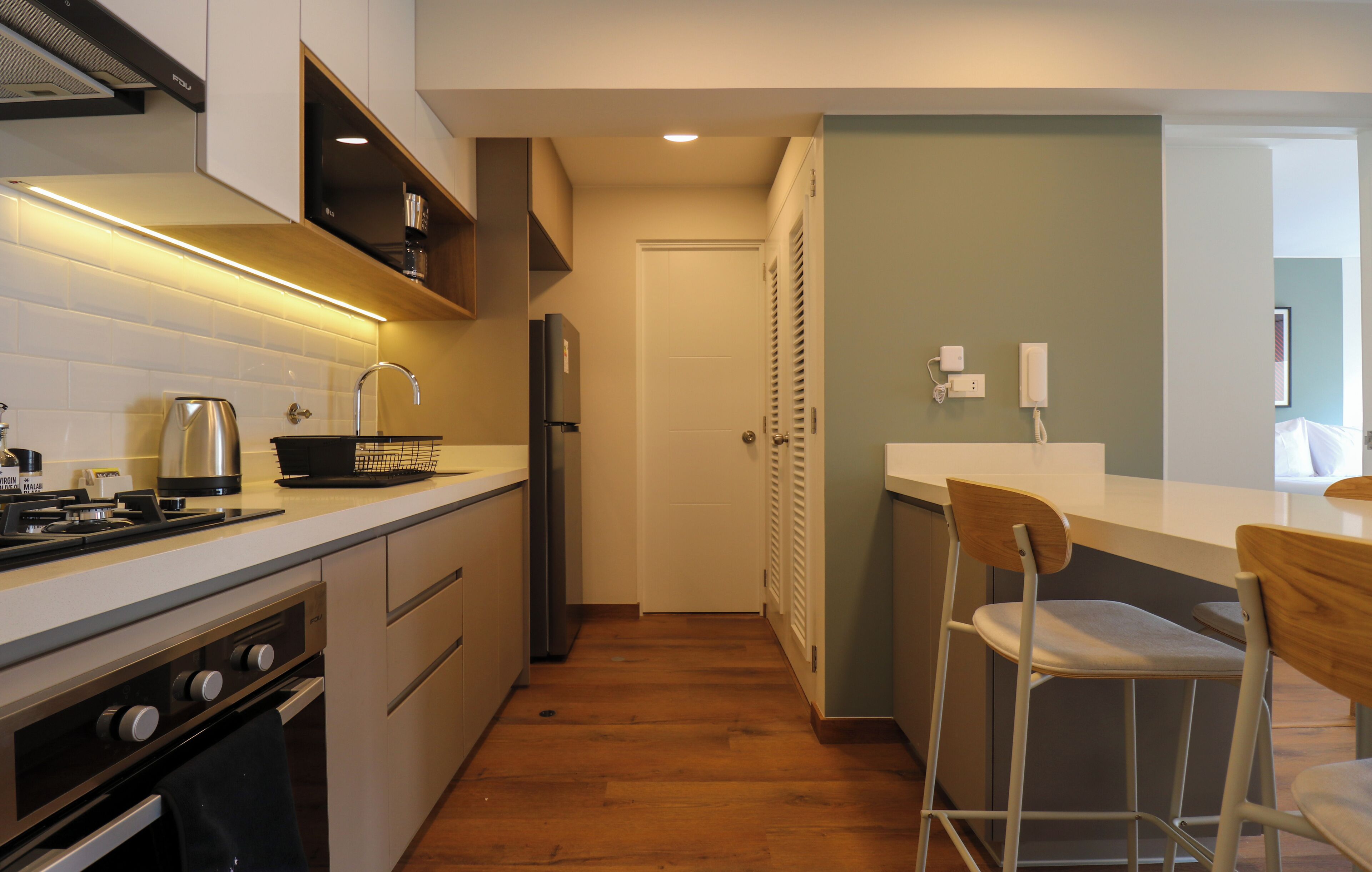 A compact kitchen with a stove, sink, and refrigerator. There is a wooden bar counter with two stools.