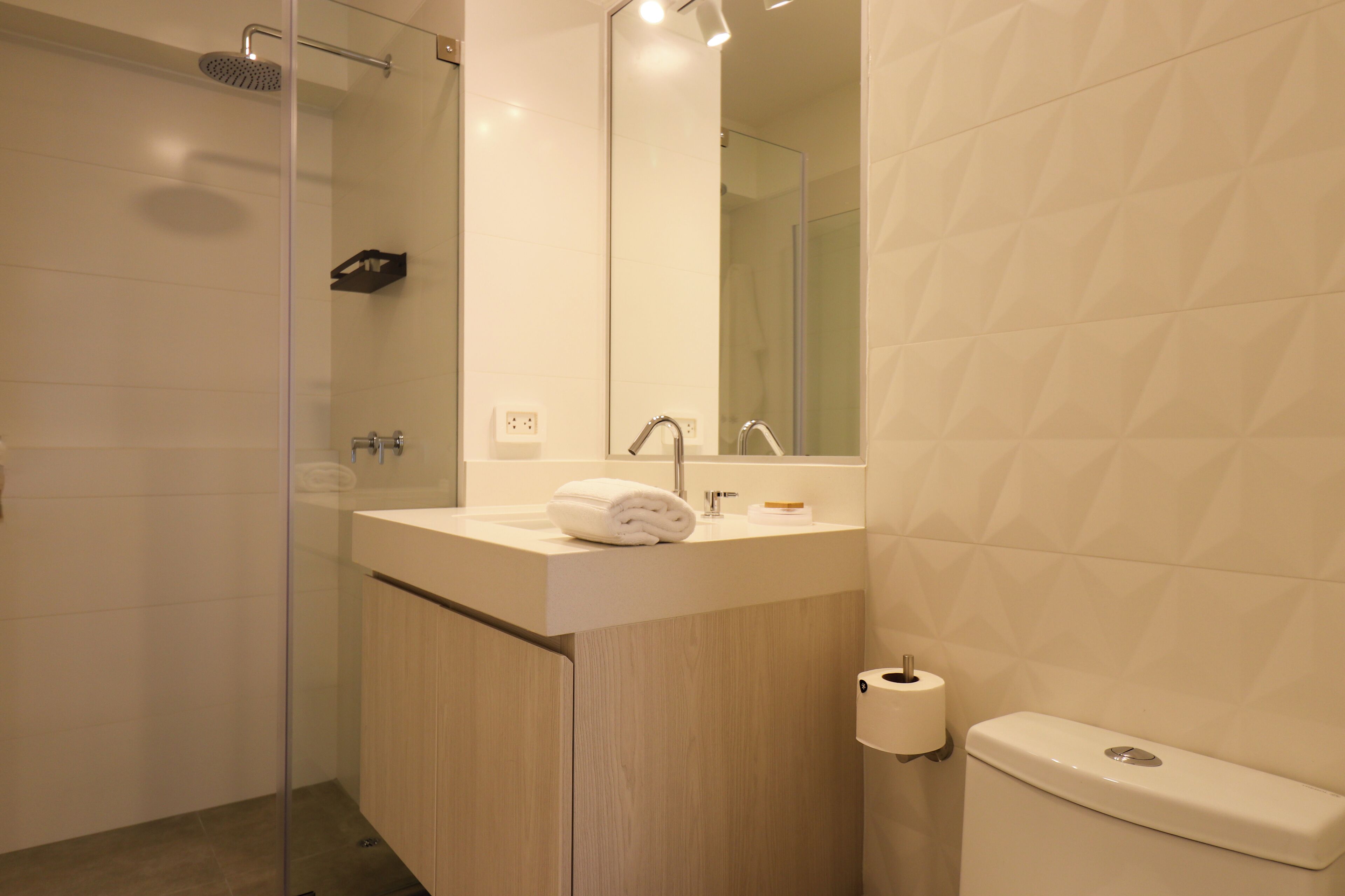 A modern bathroom with a glass shower enclosure, a wooden vanity, a white sink, and a toilet.