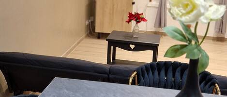 Una sala de estar moderna con una mesa de mármol, sillas tapizadas en negro, un jarrón negro con una flor blanca, un televisor de pantalla plana y un mueble de madera.