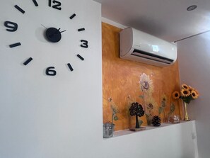 Eine moderne Wanduhr, eine Wand mit floralem Dekor und ein kleines Regal mit einer Vase voller Sonnenblumen.