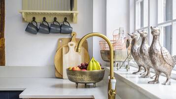 A kitchen with a white countertop, a brass faucet, a fruit bowl, a wooden cutting board, and decorative bird figurines.