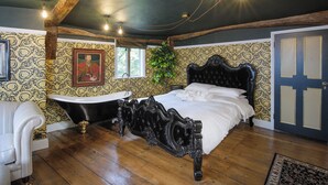 A bedroom with a large bed, a bathtub, and a wooden floor. - Luxury Rock & Roll Suite in Manor House (Saffron Walden)