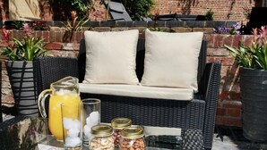 A wicker sofa with cushions, a glass table with a pitcher of orange juice, ice, and jars of nuts and dried fruits. - Luxury Rock & Roll Suite in Manor House (Saffron Walden)