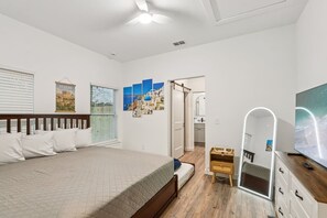 A bedroom with a bed, a wooden nightstand, a mirror, and a TV. - Stylish 3BR/2BA/6Beds • Spacious • Near Downtown (St. Augustine)