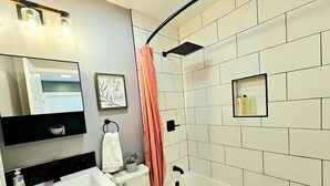 A modern bathroom with a white bathtub, a toilet, a sink, and a shower curtain. - Bright Bungalow steps from Caltech & PCC, Close to the Rose Bowl, Kingsize Bed! (Pasadena)
